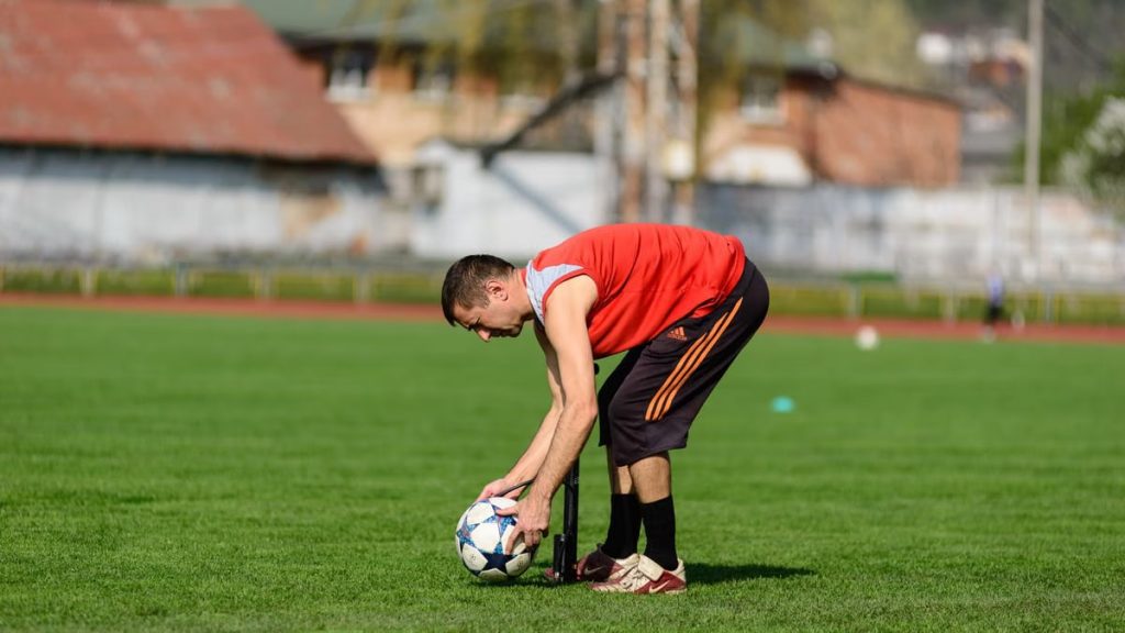 An athlete in sportswear preparing a soccer ball on a grass field during daytime training.